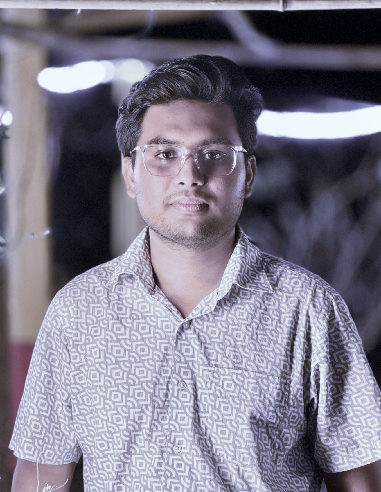 Sayman Rifat smiling in a red plaid shirt and tortoise shell glasses